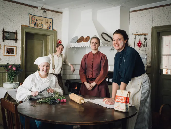 Fyra kvinnor i gammeldags kläder i kulturhistorisk miljö.