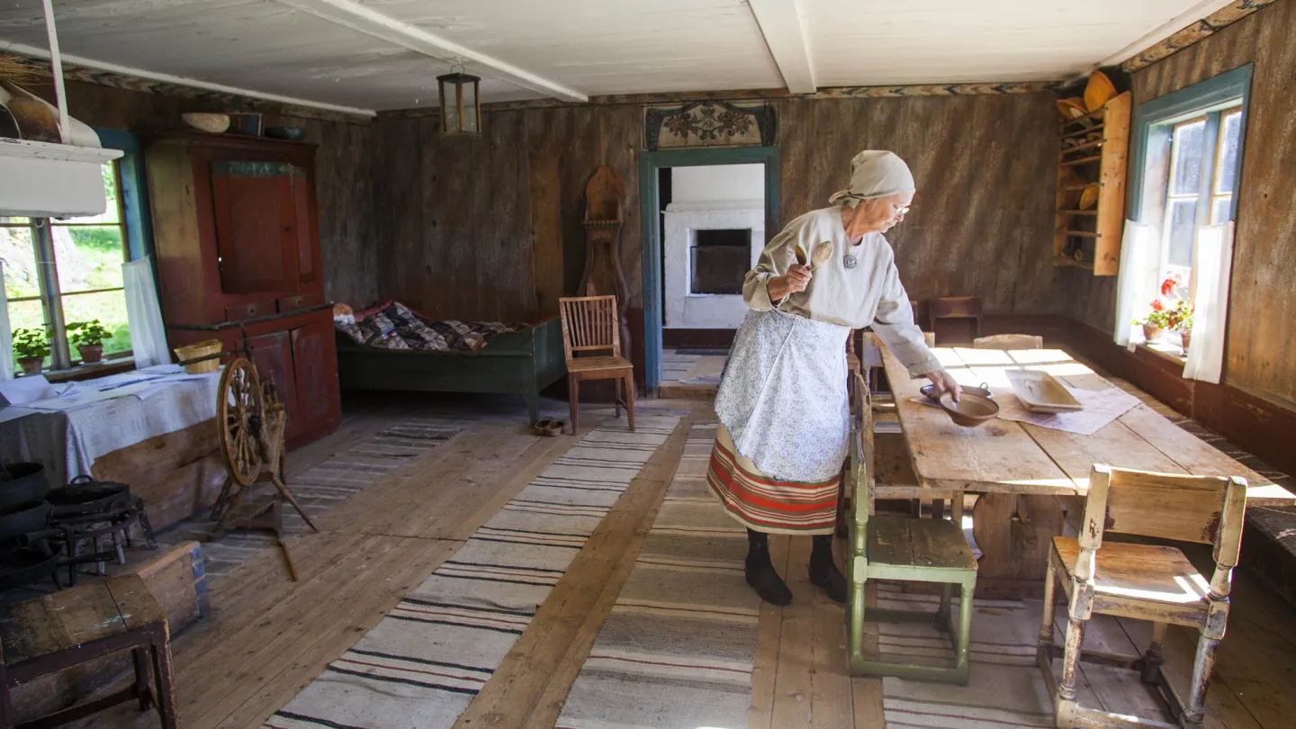 Interiör av rum i Ersk-Mats. Kvinna som dukar ett bord.