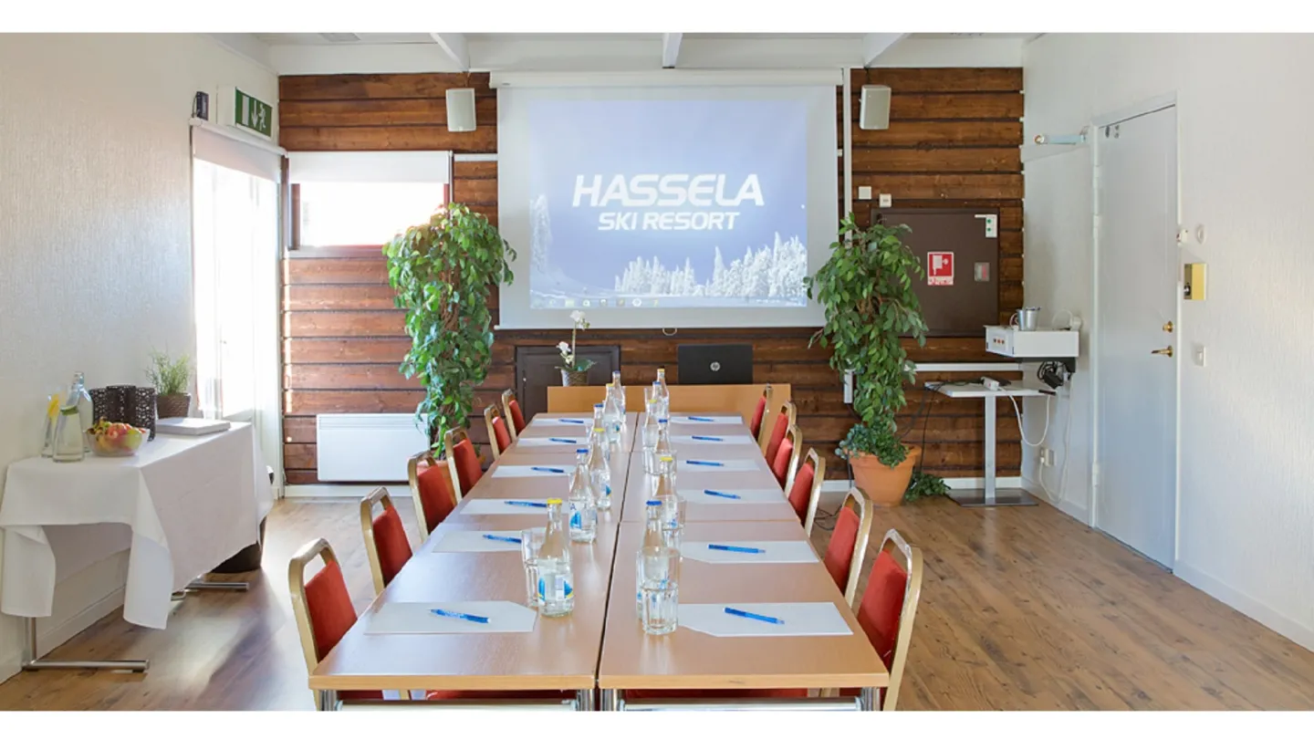 Möteslokal med bord, stolar, projektorduk på vägg, serveringsbord