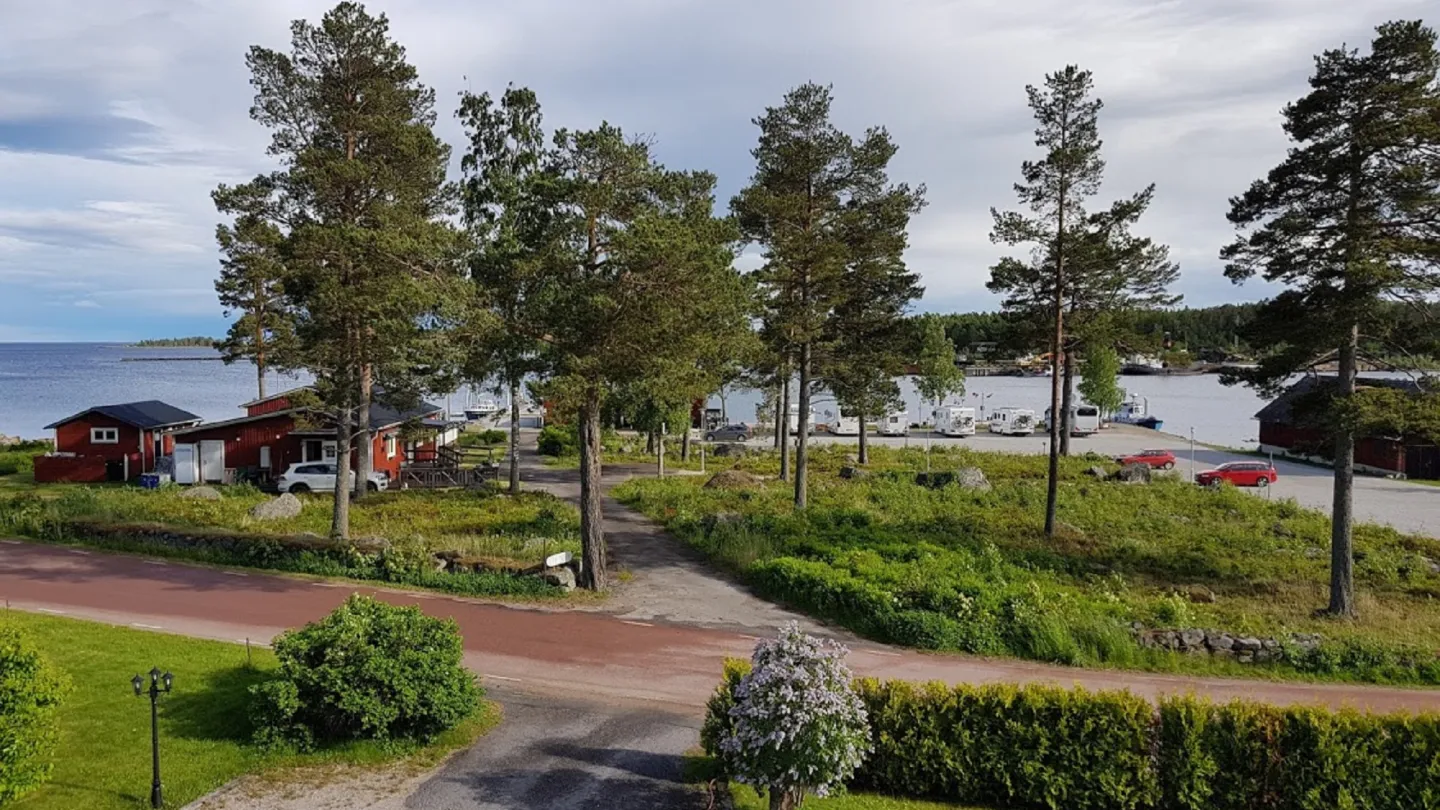 Utsikt över Stocka hamns ställplatser - husbilar vid hamnen med havet i bakgrunden, och träd i förgrunden.